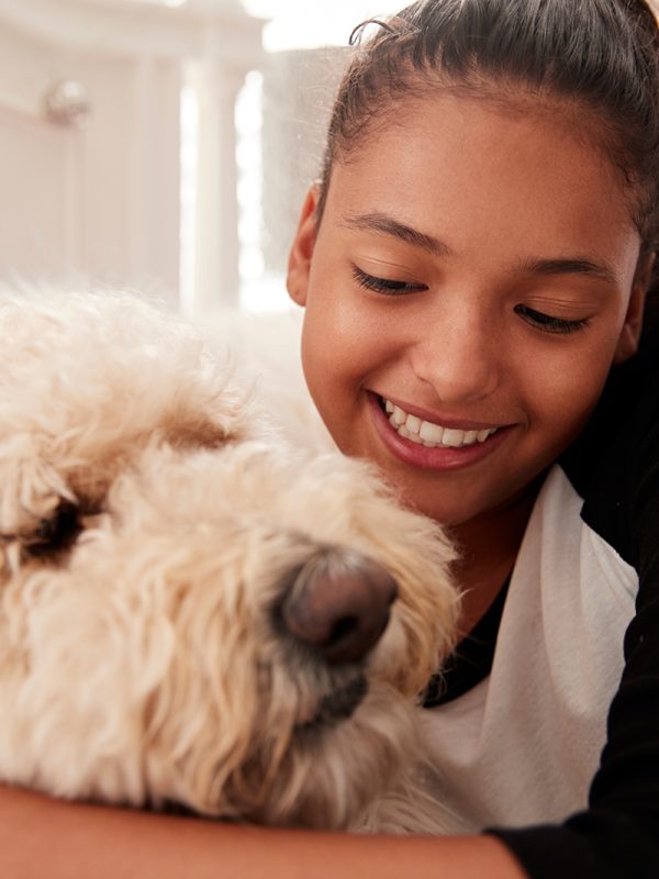 young-teen-girl-embracing-pet-dog-on-her-bed-PGQHKBW